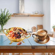 Gold bowl of assorted nuts and dried fruits next to a cup of coffee on a wooden table.