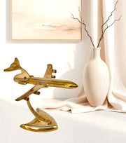 Gold airplane model on a white surface with a lamp and vase in the background